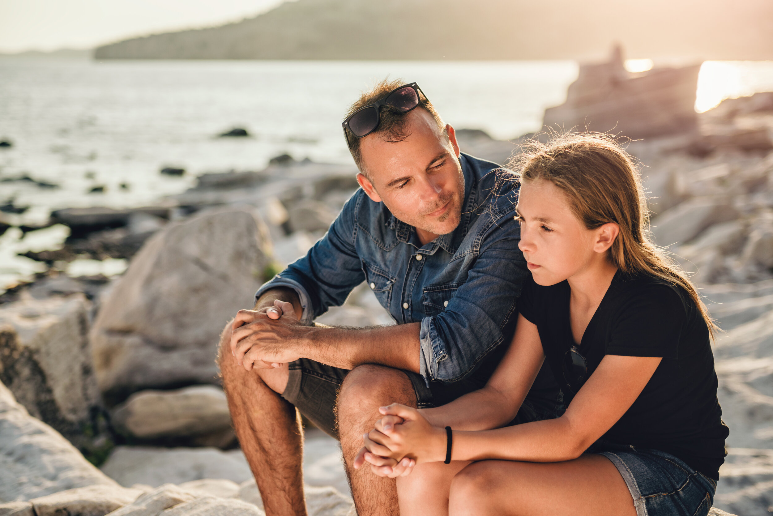 Father and daughter relaxing on a rocky beach by the sea and having time together.